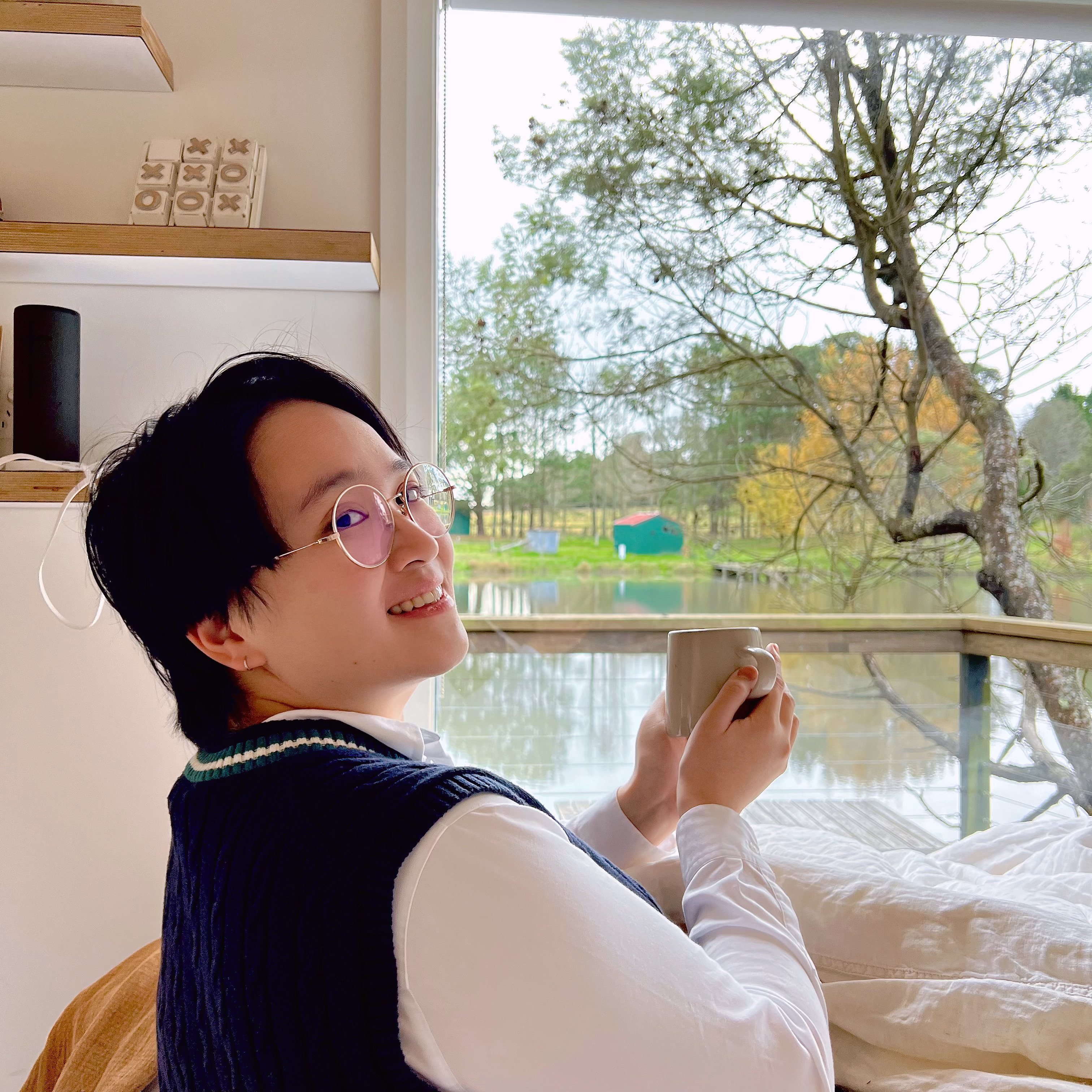 Pauline Liu sitting by a window with a cup of coffee, smiling at the camera